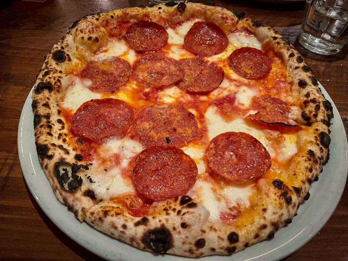 A pepperoni pizza baking in a wood-fired brick oven